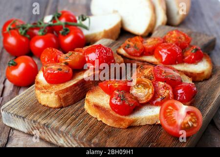 Tranches de pain grillé blanc avec tomates en conserve sur planche à découper sur table en bois, gros plan Banque D'Images