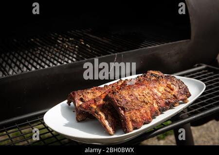 Spareribs grillés sur une plaque blanche devant le fumeur Banque D'Images