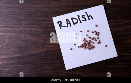 Radish graines sur un morceau de papier sur fond de bois Banque D'Images