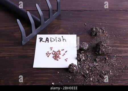 Radish graines sur un morceau de papier avec le sol et râteau sur fond de bois Banque D'Images