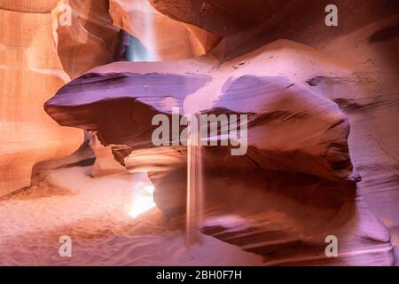 Gros plan d'un rocher de grès rouge dans le canyon Antelope, avec le sable qui coule et un faisceau de lumière du soleil tombant d'une ouverture dans la voûte Banque D'Images