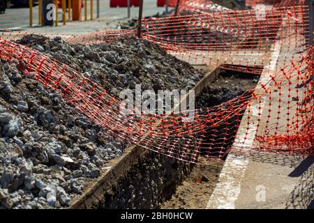 Travaux de réparation dans la rue de la ville. Une tranchée fraîchement creusée est clôturée avec un filet, pour la sécurité des citoyens Banque D'Images