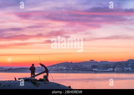 Appledore, North Devon, Angleterre. Jeudi 23 avril 2020. Météo britannique. Après une nuit douce sur l'estuaire de la rivière Torridge, un pêcheur solitaire et son chien jouissent de la paix et de la tranquillité à l'aube sur le quai d'Appledore, surplombant le village côtier d'Instow. Le soleil et une brise légère sont prévus pour le Nord Devon aujourd'hui. Crédit: Terry Mathews/Alay Live News Banque D'Images