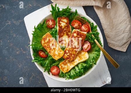 Salade végétalienne avec hallucini frits et tomates, fond sombre, vue sur le dessus Banque D'Images