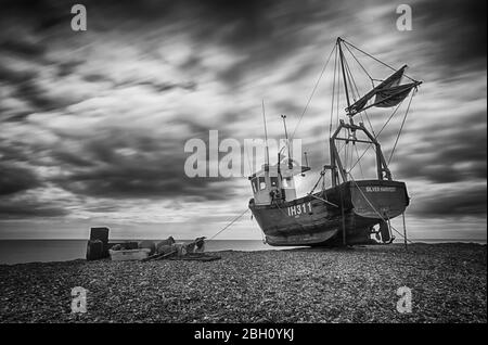 Une photo d'exposition longue d'un bateau de pêche rustique reposant sur une plage de galets à Aldborough, sur la côte du Suffolk Banque D'Images