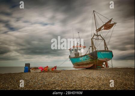 Une photo d'exposition longue d'un bateau de pêche rustique reposant sur une plage de galets à Aldborough, sur la côte du Suffolk Banque D'Images