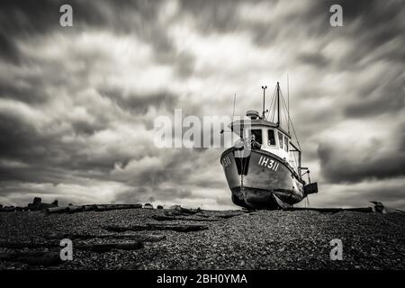 Une photo d'exposition longue d'un bateau de pêche rustique reposant sur une plage de galets à Aldborough, sur la côte du Suffolk Banque D'Images