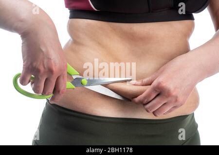 Femme d'âge moyen avec obésité et peau sagy de l'abdomen, sur fond blanc, gros plan. Ciseaux comme symbole de la rétraction chirurgicale. Banque D'Images