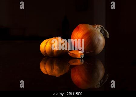 Gros plan sur la paillasse de la cuisine avec de l'ail et de l'oignon. Ustensiles de cuisine instinctifs dans le fond sombre. Banque D'Images