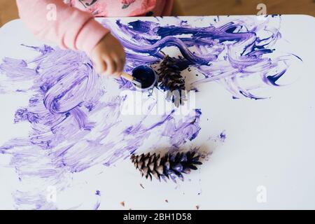 Vue rapprochée de la main de bébé-tout-petit pour faire des taches avec de la peinture violette sur la table. Banque D'Images