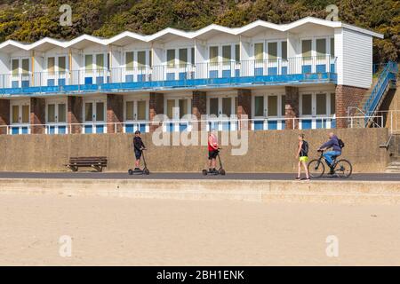 Poole, Dorset Royaume-Uni. 23 avril 2020. Temps au Royaume-Uni: Belle journée chaude et ensoleillée comme les températures augmentent sur les plages de Poole sur la côte sud que les gens prennent leur exercice autorisé, la plupart en respectant les directives du coronavirus et de la distanciation sociale . Différents modes de transport sur la promenade passant des huttes de plage à Branksome Chine - hommes à cheval scooters électriques, scooter électrique, à vélo, femme marchant. Crédit : Carolyn Jenkins/Alay Live News Banque D'Images