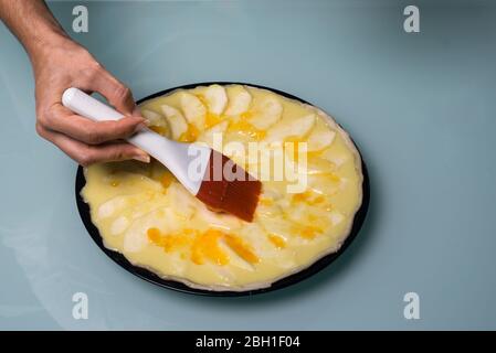 Travail dans la cuisine. Détail des mains frottant la confiture de pêche sur le gâteau. Préparation de la cuisson. Faire cuire la tarte aux pommes. Brosse. Ingrédients culinaires. Gâteau aux fruits. Ki Banque D'Images