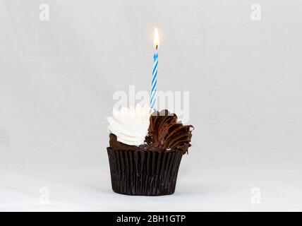 Un cupcake brun et blanc avec une bougie d'anniversaire à rayures bleues et blanches brûlant sur le dessus. Banque D'Images