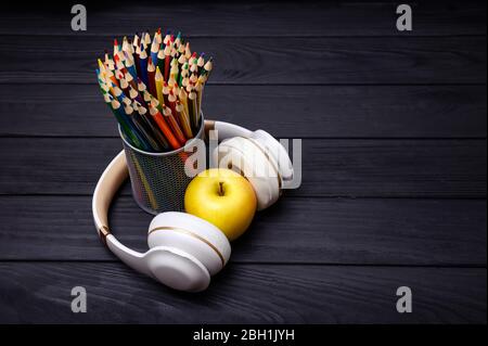 Crayons et écouteurs colorés sur fond noir en bois. Lieu de travail Banque D'Images