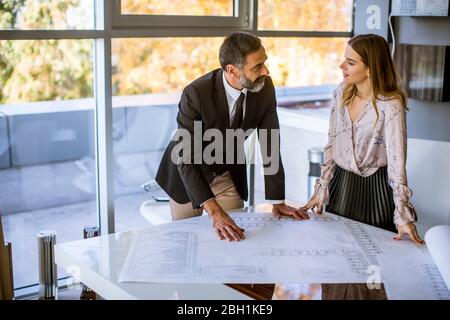 Beau architecte et sa jeune collègue de sexe féminin vérifiant les plans et les plans dans le bureau Banque D'Images