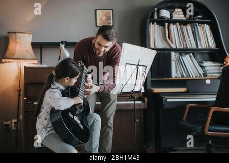 Jolie petite fille jouant de la guitare avec son professeur de musique dans l'appartement rustique Banque D'Images