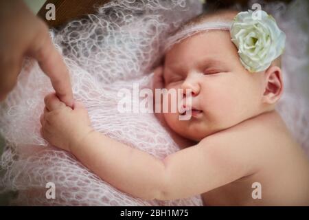 un bébé nouveau-né charmant avec une fleur sur sa tête dort sur un plaid en maille rose tient le doigt de mamans Banque D'Images