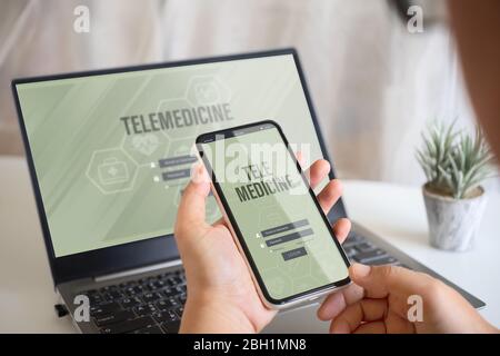 Concept de contexte d'application en ligne de télémédecine. Mockup téléphone mobile et ordinateur portable, une personne qui tient son smartphone à l'aide de l'application système de télémédecine Banque D'Images