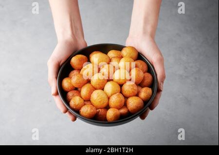 Loukoumades ou luqaimat ou lokma dans un bol noir dans les mains des femmes sur fond gris . Loukoumades est un donunts de cuisine orientale populaire pendant Ramazan. Po Banque D'Images