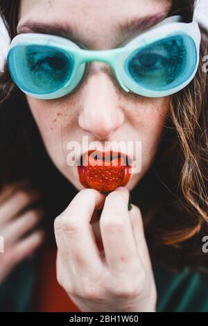 Portrait d'une femme portant des lunettes de plongée bleues mangeant de la fraise Banque D'Images