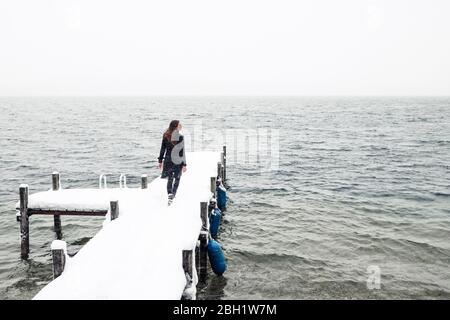 Vue arrière de la jeune femme marchant sur une jetée enneigée au lac Starnberg, Allemagne Banque D'Images