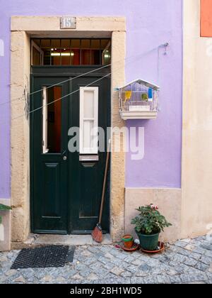 Porte typique d'une maison dans les rues latérales du quartier de la vieille ville de Lisbonne, Portugal, avec un oiseau de compagnie chantant dans sa cage. Banque D'Images