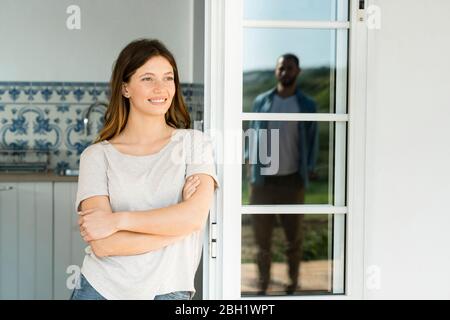 Jeune femme souriante se penchée sur la porte en regardant son petit ami debout à l'extérieur Banque D'Images