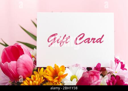 Carte cadeau en bouquet de fleurs sur fond rose. Carte cadeau bon cadeau pour femme. Bon surprise pour la fête des mères, l'anniversaire ou l'anniversaire Banque D'Images