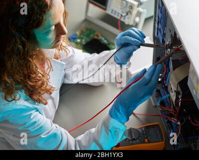 Technicienne féminine travaillant sur ordinateur ouvert, à l'aide d'un appareil de mesure Banque D'Images