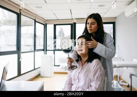 Chirurgien cosmétique tenant le miroir et parlant au patient dans la pratique médicale Banque D'Images