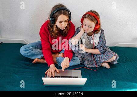 Portrait de deux sœurs avec casque assis sur le lit et regardant un ordinateur portable Banque D'Images