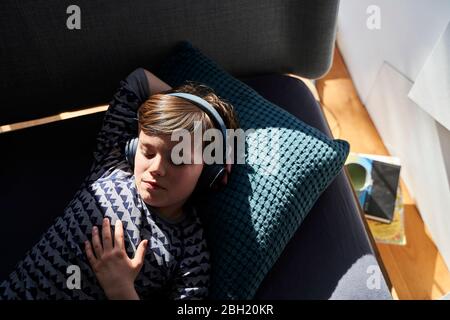 Portrait d'un garçon allongé sur un canapé écoutant de la musique avec un casque Banque D'Images