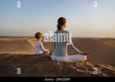 Mère et fille pratiquant le yoga dans les dunes de sable au coucher du soleil, Gran Canaria, Espagne Banque D'Images