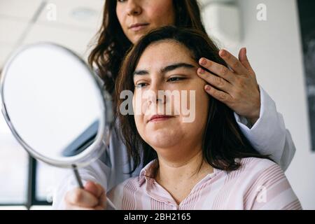 Chirurgien cosmétique tenant le miroir et parlant au patient dans la pratique médicale Banque D'Images