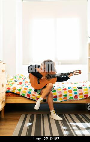 Garçon assis sur le lit à la maison jouant de la chanson sur la guitare Banque D'Images