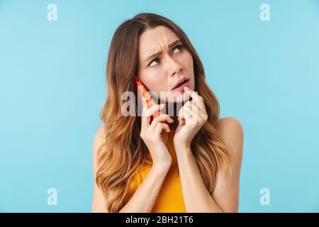 Portrait de la jeune femme caucasienne belle soulignant tout en parlant sur téléphone portable isolé sur fond bleu en studio Banque D'Images