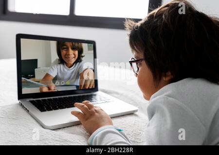 Petit garçon allongé sur le lit en utilisant un ordinateur portable pour le chat vidéo Banque D'Images