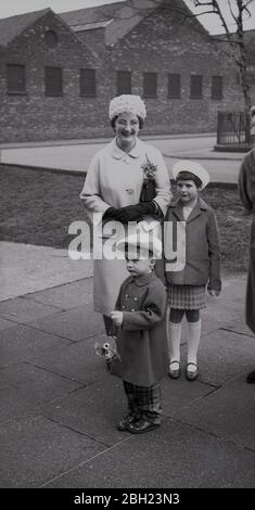 1962, historique, deux enfants avec leur grand-mère qui assistent à un mariage avec le petit garçon à la mode portant un cap, vérifier le pantalon « Rupbert the Bear », une casquette « working mans » et tenir un flash pour un appareil photo, Angleterre. ROYAUME-UNI. Banque D'Images