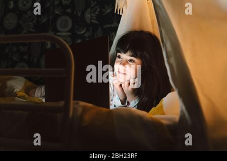 Portrait d'une fille souriante, allongé sur le lit et regardant un ordinateur portable Banque D'Images