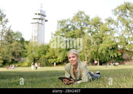 Portrait d'une femme couché sur un pré avec une tablette numérique Banque D'Images