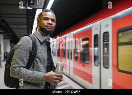 Homme élégant avec tasse réutilisable et écouteurs dans une station de métro Banque D'Images