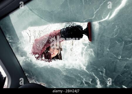 Portrait d'une jeune femme qui nettoie la neige du pare-brise de la voiture Banque D'Images