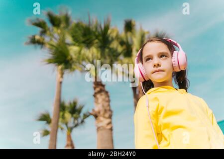 Portrait d'une petite fille sérieuse écoutant de la musique avec des écouteurs à l'extérieur Banque D'Images