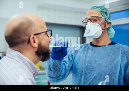 Médecin à l'hôpital prenant un écouvillon de la bouche du patient Banque D'Images