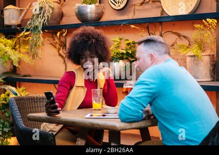 Homme et femme prenant un verre dans un restaurant, en utilisant un smartphone
