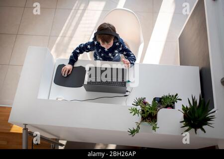 Vue de dessus d'un garçon assis au bureau à la maison, avec un casque et un ordinateur portable Banque D'Images