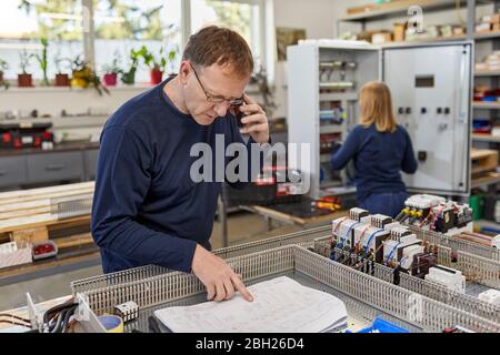 Homme au téléphone pour vérifier le schéma électrique dans l'atelier électrique Banque D'Images