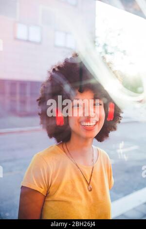 Portrait de la jeune femme heureuse avec des cheveux afro écouter de la musique avec des écouteurs dans la ville Banque D'Images