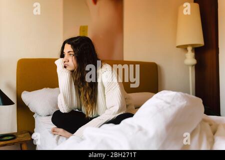 Portrait de la triste fille assise sur le lit regardant la distance Banque D'Images
