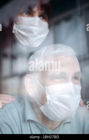 Portrait d'un couple âgé portant des masques à la maison, regardant par la fenêtre Banque D'Images